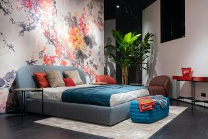 bed with blue, red, and white bedding and a floral accent wall behind