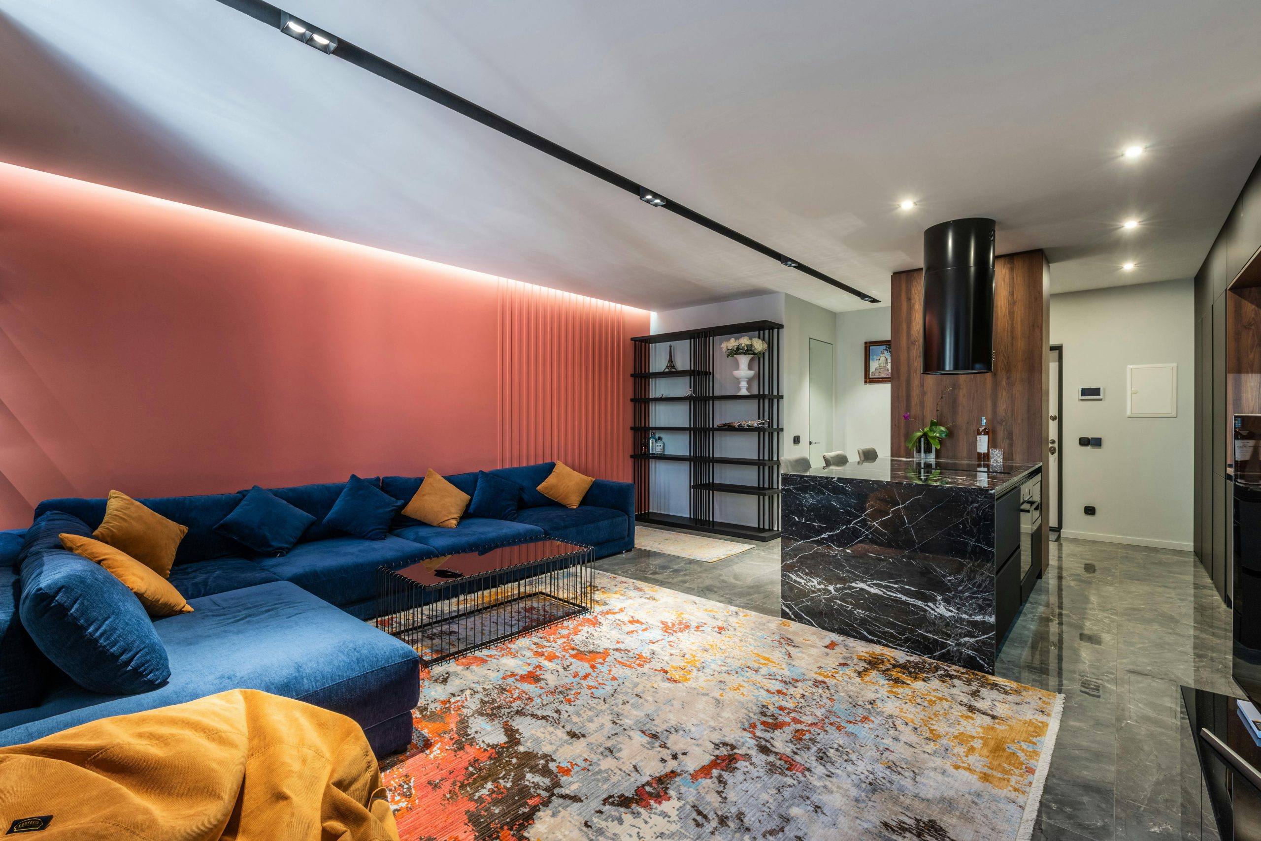 living room with white walls and ceiling, orange accent wall, blue couch, and patterned carpet