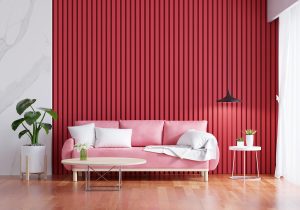 a blush pink couch, an off-white coffee table, and indoor plants, with a red batten accent wall behind